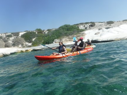 Drei Kajakfahrer paddeln in klarem Wasser, umgeben von einer malerischen Küstenlandschaft mit weißen Felsen.