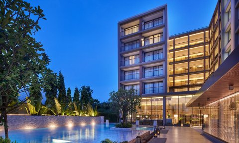 Ein elegantes Hotelgebäude mit beleuchteten Balkonen, umgeben von üppigem Grün und einem glitzernden Pool bei Dämmerung.