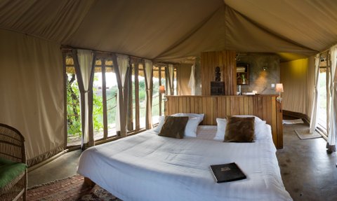 Ein elegantes Zeltinnere mit einem großen Bett, umgeben von Fenstern, die einen Blick auf die Natur bieten.