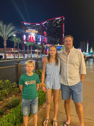 Eine Familie steht lächelnd vor den hell erleuchteten Gebäuden von Las Vegas, umgeben von Palmen und nächtlicher Atmosphäre.