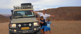 Eine Mutter steht mit ihren beiden Söhnen neben einem Jeep - Namibia Rundreise mit Kindern