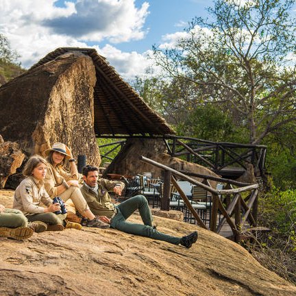Eine Gruppe von vier Personen sitzt entspannt auf einem Felsen und genießt die Aussicht auf die Natur und die Wolken.
