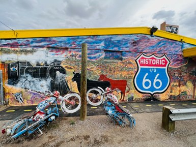 Eine bunte Wandmalerei zeigt eine Dampflok und das historische Schild der Route 66, umgeben von nostalgischen Motiven.