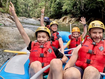 Familie im Schlauchboot lächelt in die Kamera, während sie den Fluss hinunterfährt – Malaysia & Borneo Familienreise