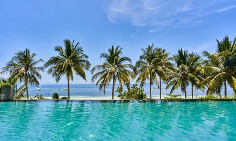Kristallklares Wasser des Pools reflektiert die Palmen und das strahlend blaue Himmel über dem ruhigen Meer.