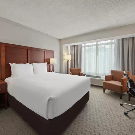 Ein modernes Hotelzimmer mit einem großen Bett, eleganten Möbeln und viel natürlichem Licht durch große Fenster.