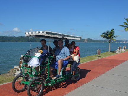 Eine Gruppe von fünf Personen sitzt in einem grünen Fahrrad-Rikschawagen am Amador Causeway in Panama City.