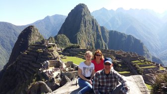 Drei Personen posieren fröhlich vor der beeindruckenden Kulisse von Machu Picchu, umgeben von majestätischen Bergen.