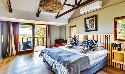 Ein stilvolles Schlafzimmer mit einem großen Bett, dekorativen Kissen und einem Blick auf die Natur durch große Fenster.