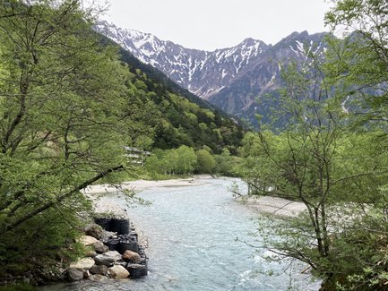 Ein klarer Fluss schlängelt sich durch eine grüne Landschaft, umgeben von schneebedeckten Bergen im Hintergrund.
