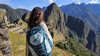 Eine Person mit einem Rucksack steht an einem Aussichtspunkt und blickt auf die beeindruckenden Ruinen von Machu Picchu.