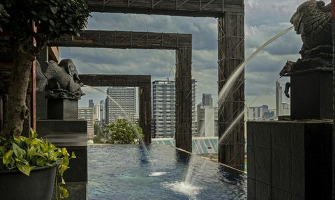 Ein Blick auf einen stilvollen Außenpool mit Wasserspielen und modernem urbanen Hintergrund in Bangkok.
