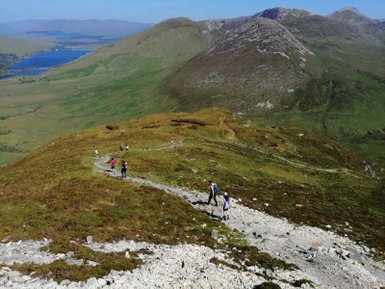 Eine Gruppe von Wanderern erkundet den Diamond Hill im Connemara Nationalpark, umgeben von grünen Hügeln und blauen Seen.