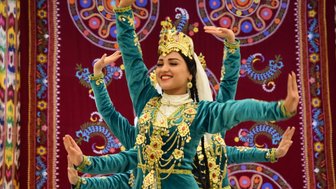 Eine Tänzerin in traditioneller Kleidung lächelt, während sie mit anmutigen Bewegungen auf einer Bühne tanzt.