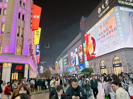 Eine belebte Einkaufsstraße in Shanghai, erleuchtet von bunten Reklametafeln und umgeben von Menschenmengen.