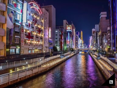 Die nächtliche Skyline von Osaka spiegelt sich im ruhigen Wasser eines Kanals, umgeben von bunten Neonlichtern und Gebäuden.