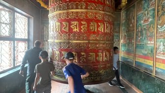 Eine Gruppe von Kindern und Erwachsenen dreht gemeinsam eine große Gebetsmühle in einem buddhistischen Tempel in Nepal.