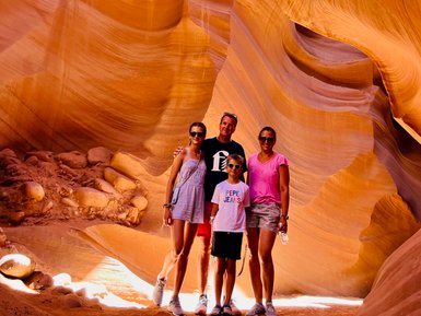 Eine Familie steht in der beeindruckenden Antelope Canyon, umgeben von orangefarbenen Sandsteinformationen und weichem Licht.