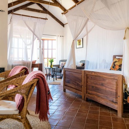 Ein helles Schlafzimmer mit zwei Betten, umgeben von weißen Moskitonetzen und rustikalen Holzmöbeln.