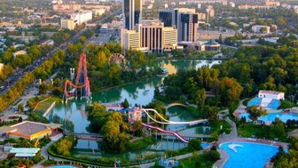 Eine Luftaufnahme von Taschkent zeigt einen lebhaften Park mit Fahrgeschäften, Schwimmbädern und grünen Bäumen.