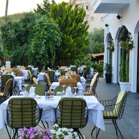 Eine einladende Terrasse mit eleganten Tischen und Stühlen, umgeben von üppigem Grün und blühenden Pflanzen.
