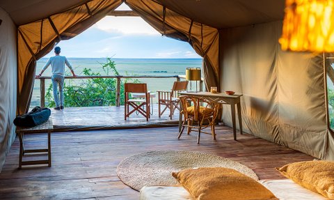 Ein Mann steht entspannt auf der Veranda eines Zeltes und blickt über die weite Landschaft des Ngorongoro-Kraters.