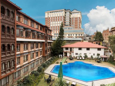 Ein einladender Pool umgeben von gepflegten Gärten und modernen Gebäuden, ideal für Familienurlaube in Nepal.