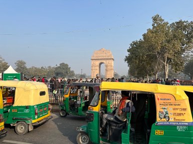 Bunte Tuk-Tuks stehen in der Nähe des India Gate, umgeben von einer Menschenmenge und Bäumen unter klarem Himmel.