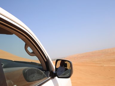 Beduine in der Wahiba-Wüste spiegelt sich im Außenspiegel des Autos – Oman Reise mit Kindern