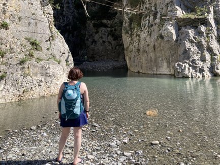 Eine Person steht am Ufer eines klaren Gewässers, umgeben von hohen, steilen Felsen und einer malerischen Landschaft.