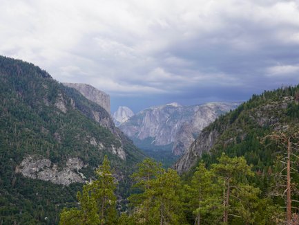 Ein atemberaubender Blick auf die majestätischen Berge des Yosemite-Nationalparks, umgeben von dichten Wäldern und dramatischen Wolken.