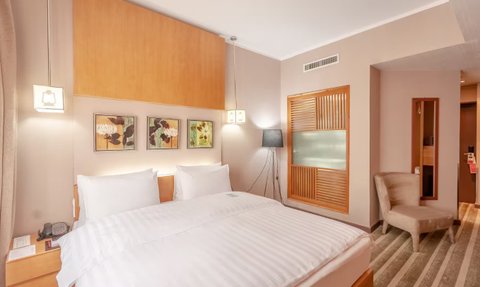 Ein modernes Hotelzimmer mit einem großen Doppelbett, sanften Farben und stilvollen Wandbildern, die eine entspannende Atmosphäre schaffen.