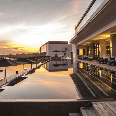 Ein eleganter Poolbereich mit Sonnenschirmen, der in den Sonnenuntergang über einer üppigen Landschaft blickt.