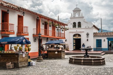 Der lebhafte Stadtplatz in Medellín zeigt bunte Stände mit frischen Früchten und handgefertigten Waren unter einem bewölkten Himmel.