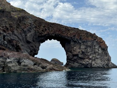 Ein beeindruckender Felsbogen erhebt sich über das ruhige Wasser, umgeben von schroffen Klippen und einem klaren Himmel.