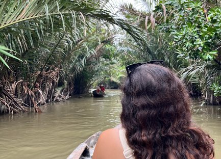 Eine Person mit lockigem Haar sitzt in einem Boot und genießt die ruhige Fahrt durch einen grünen Wasserweg im Mekong-Delta.