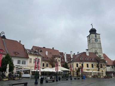Der Platz in Sibiu zeigt historische Gebäude mit roten Dächern und einem markanten Uhrturm unter einem grauen Himmel.