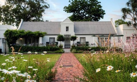 Ein charmantes Cottage mit einem begrünten Garten, umgeben von bunten Blumen und einem gepflasterten Weg.