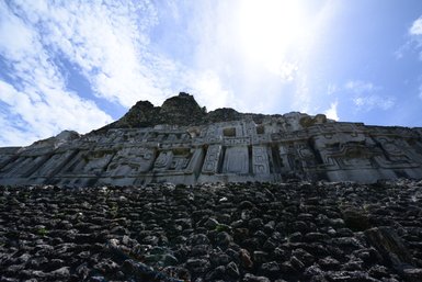 Die beeindruckende Fassade eines alten Maya-Tempels, umgeben von steilen Steinen und unter einem strahlend blauen Himmel.