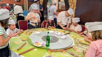 Eine Gruppe von Kindern und einem Koch bereitet gemeinsam Jiaozi in einer lebhaften Restaurantküche vor.