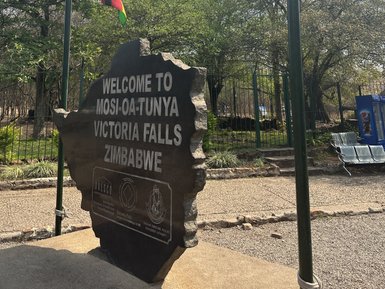 Ein markantes Steinschild begrüßt Besucher am Eingang zu den Victoriafällen in Zimbabwe, umgeben von üppigem Grün.
