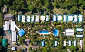 Eine Luftaufnahme eines tropischen Hotels mit blauen Dächern, umgeben von üppigem Grün und einem Pool in der Mitte.