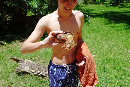 Ein junger Mann hält eine große Schnecke in der Hand und lächelt, während er auf einer grünen Wiese steht.