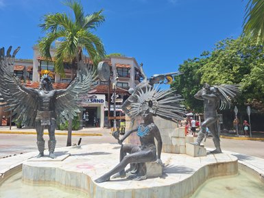 Eine beeindruckende Statue mit drei Figuren, die traditionelle mexikanische Tänze darstellen, umgeben von einem lebhaften Stadtbild.