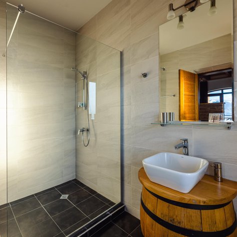 Ein modernes Badezimmer mit einer gläsernen Dusche und einem Waschbecken auf einem Holzfass, das rustikalen Charme ausstrahlt.