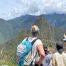 Eine Gruppe von Menschen steht auf einem Aussichtspunkt und bewundert die Ruinen von Machu Picchu inmitten der Berge.