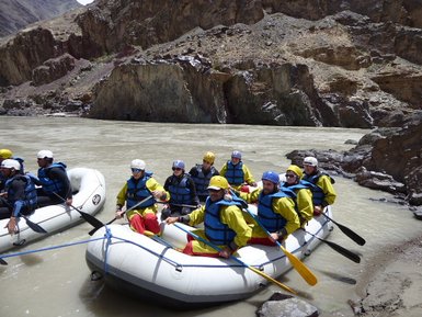 Eine Gruppe von acht Personen in Neoprenanzügen sitzt in einem Schlauchboot auf einem reißenden Fluss, umgeben von steilen Felsen.