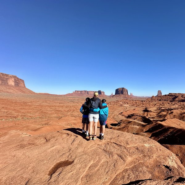 Drei Personen stehen auf einem roten Felsen und blicken auf die beeindruckende Landschaft von Monument Valley.