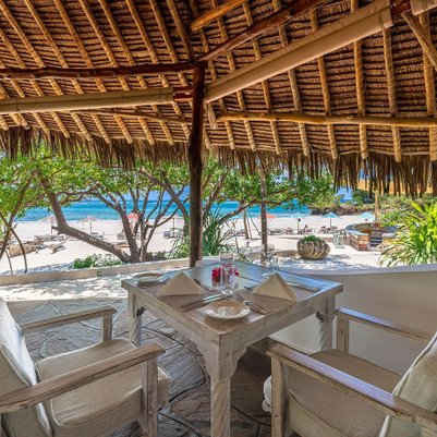 Ein einladender Restaurantbereich mit Blick auf den Strand, umgeben von üppigem Grün und einem klaren blauen Meer.