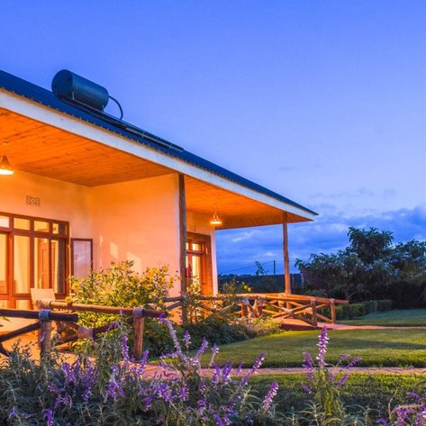 Ein modernes Haus mit Holzveranda, umgeben von bunten Blumen und sanften Hügeln, erleuchtet im sanften Abendlicht.